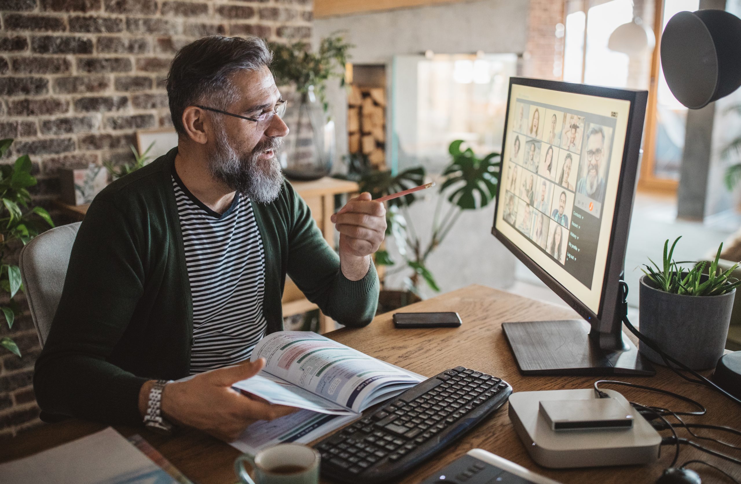 A middle-aged white male with a full beard works at a desktop computer and points at the screen with a pencil in a moment of sudden realization.