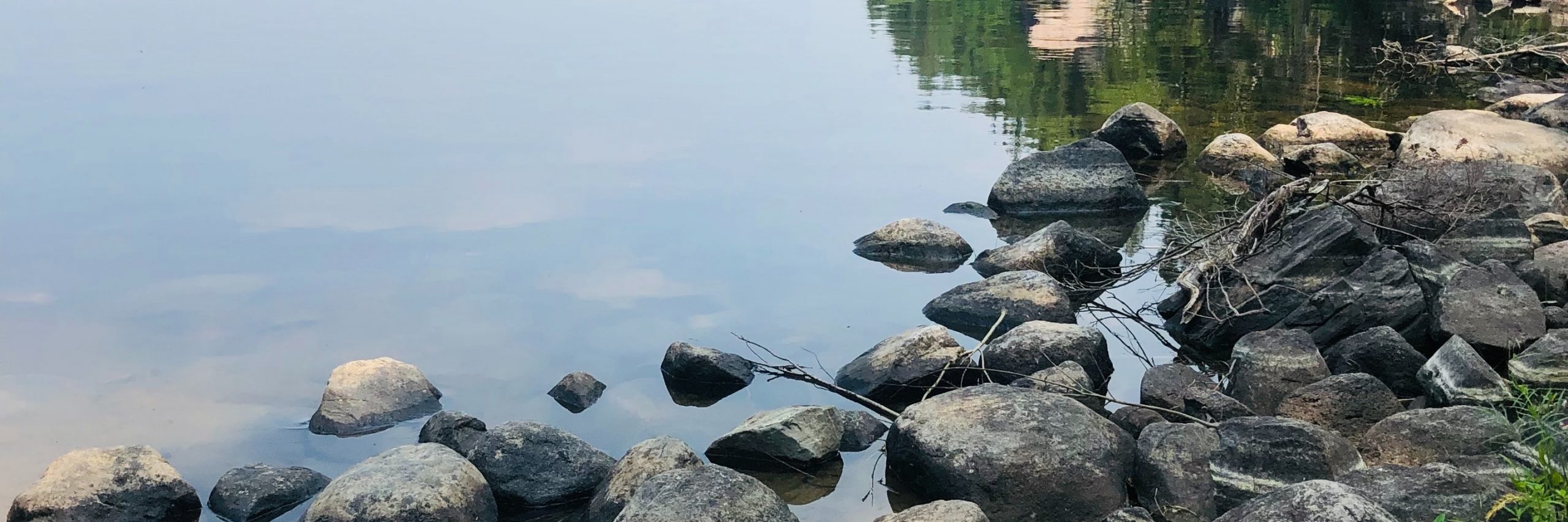 Still lake water surrounds the large black rock along shore of Nopiming Provincial Park in Manitoba