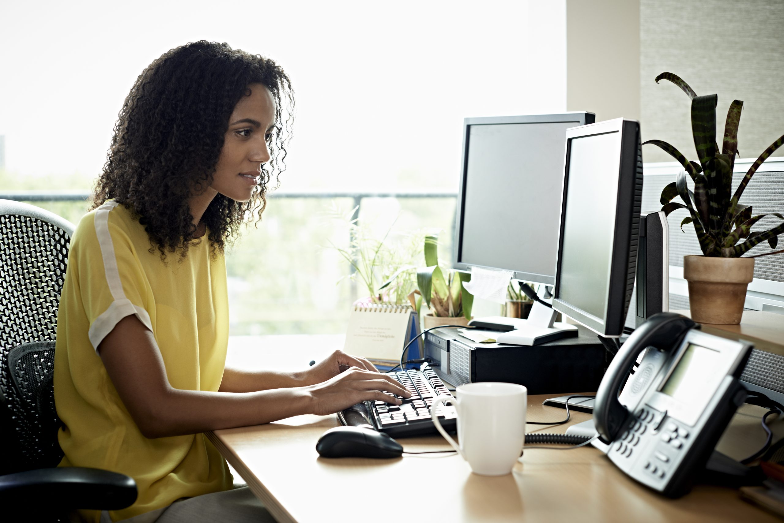 Black woman attentively using a desktop computer in a modern office.