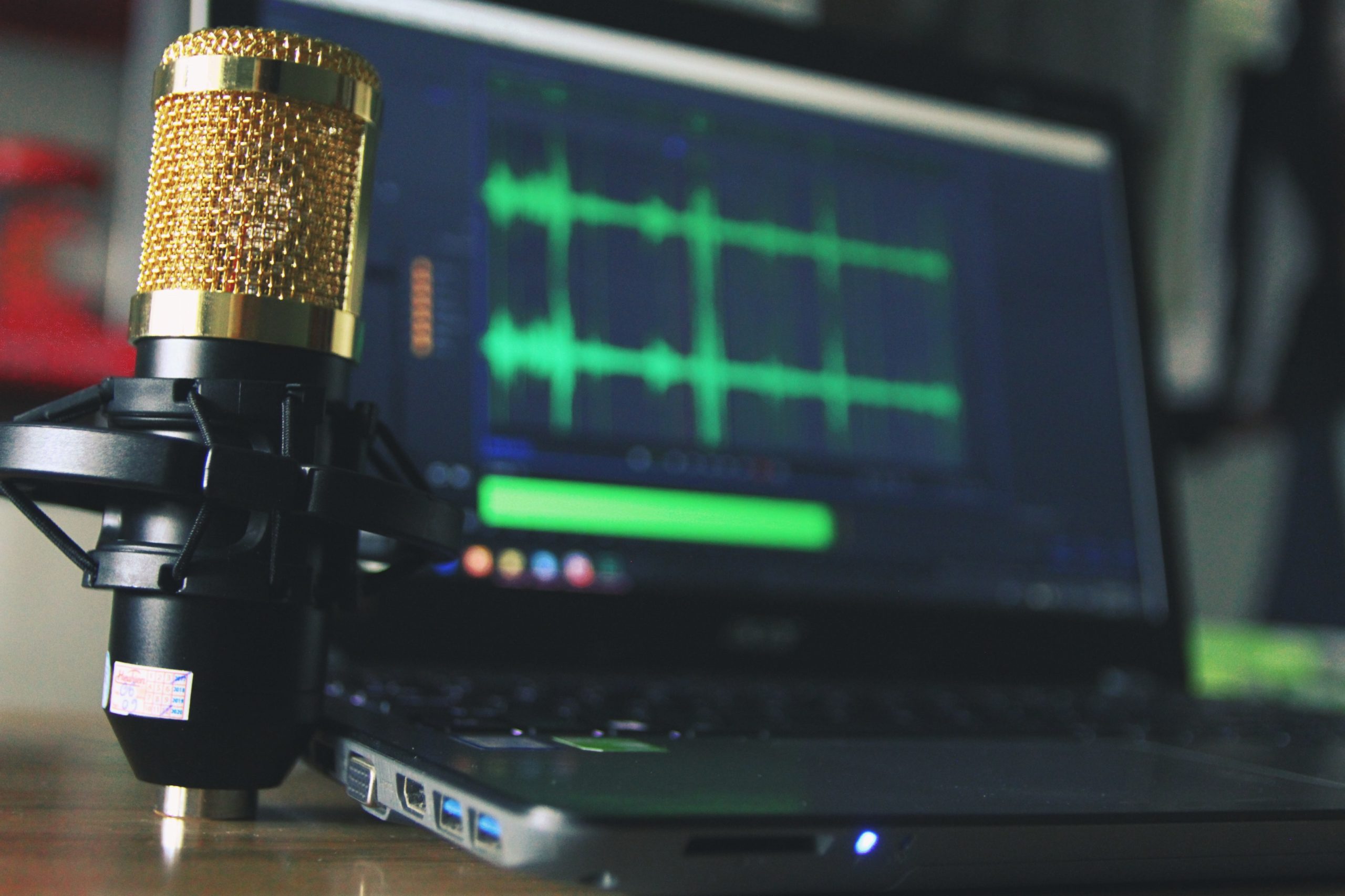 A gold condenser microphone near black laptop computer which is displaying voice tracks.