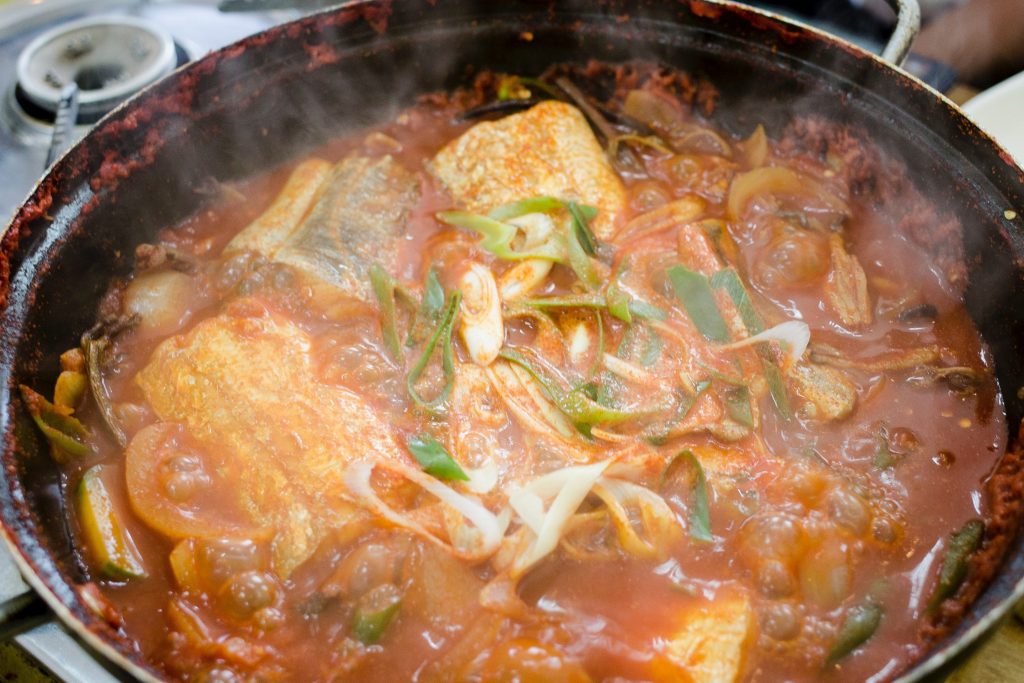 Spicy fish soup with vegetable in wok on a table top.