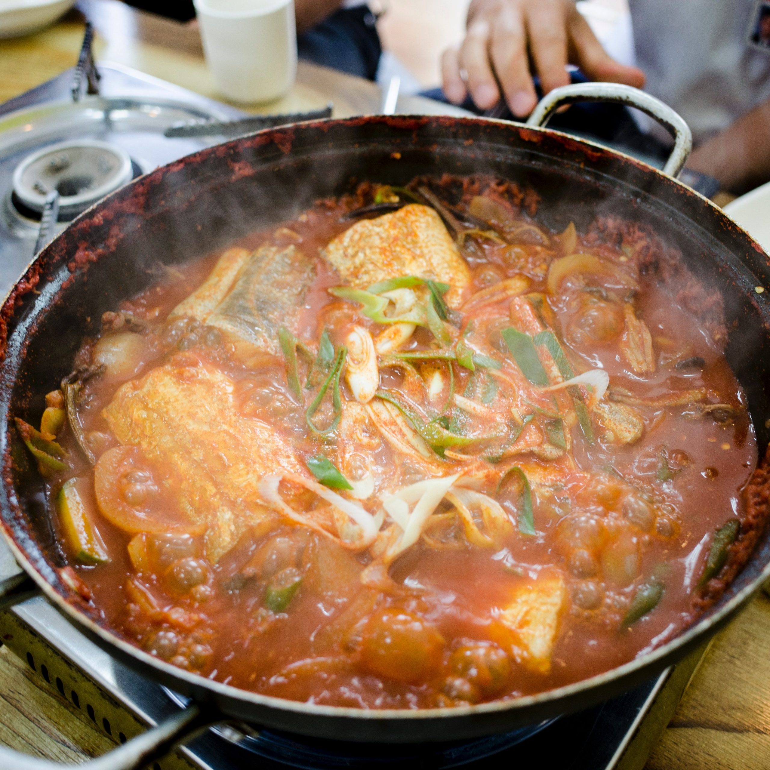 Spicy fish soup with vegetable in wok on a table top.