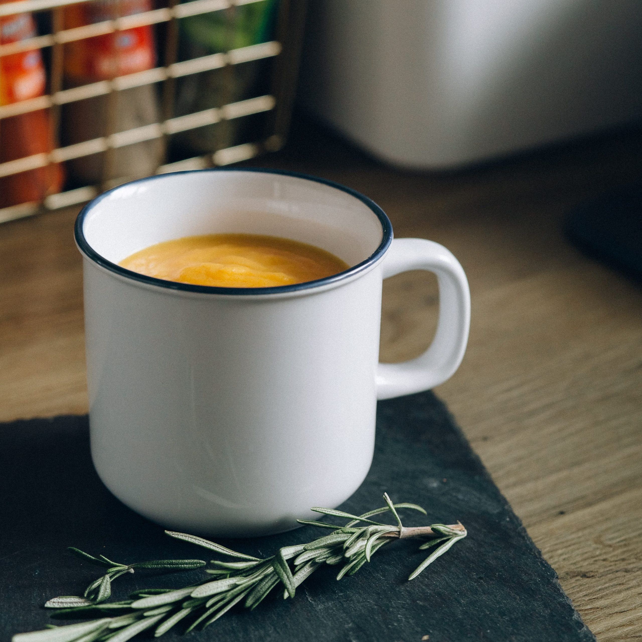 Pumpkin soup in a white enamel mugs sits on a wooden counter