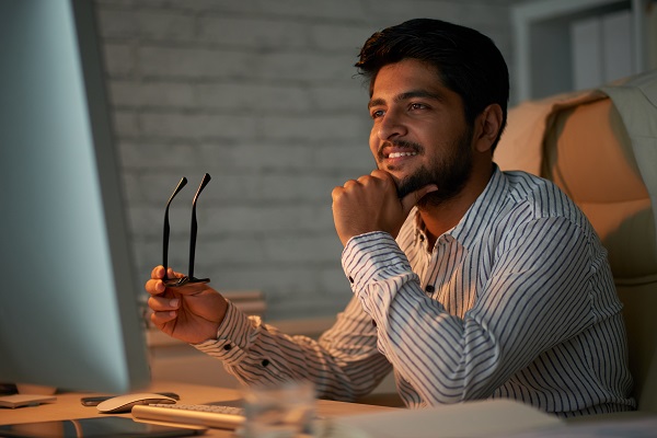 Smiling handsome Indian entreprenur reading information on computer screen