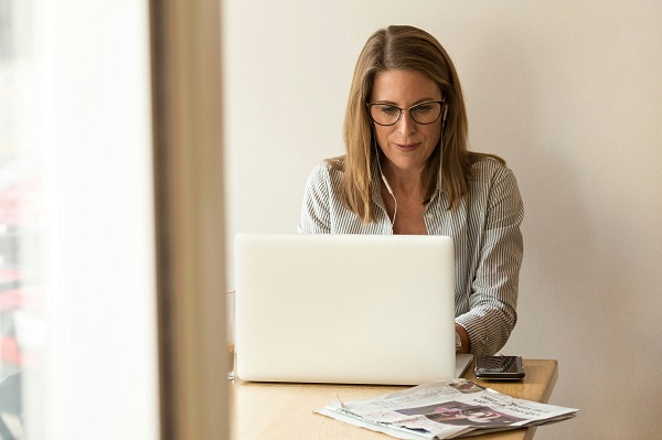 A middle-aged white woman uses a laptop on a wooden table.