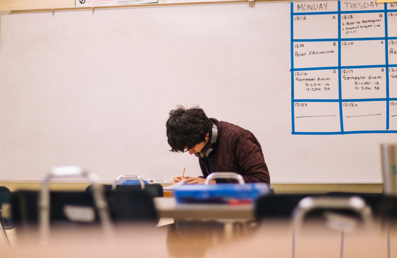 Student writing test in empty classroom, head bent over paper test