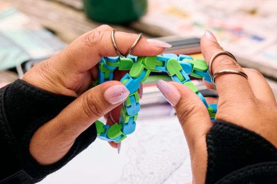 Close-up of an Indigenous woman’s hands using a fidget stim. The woman wears finger splints on her index fingers and support wraps around her wrists.