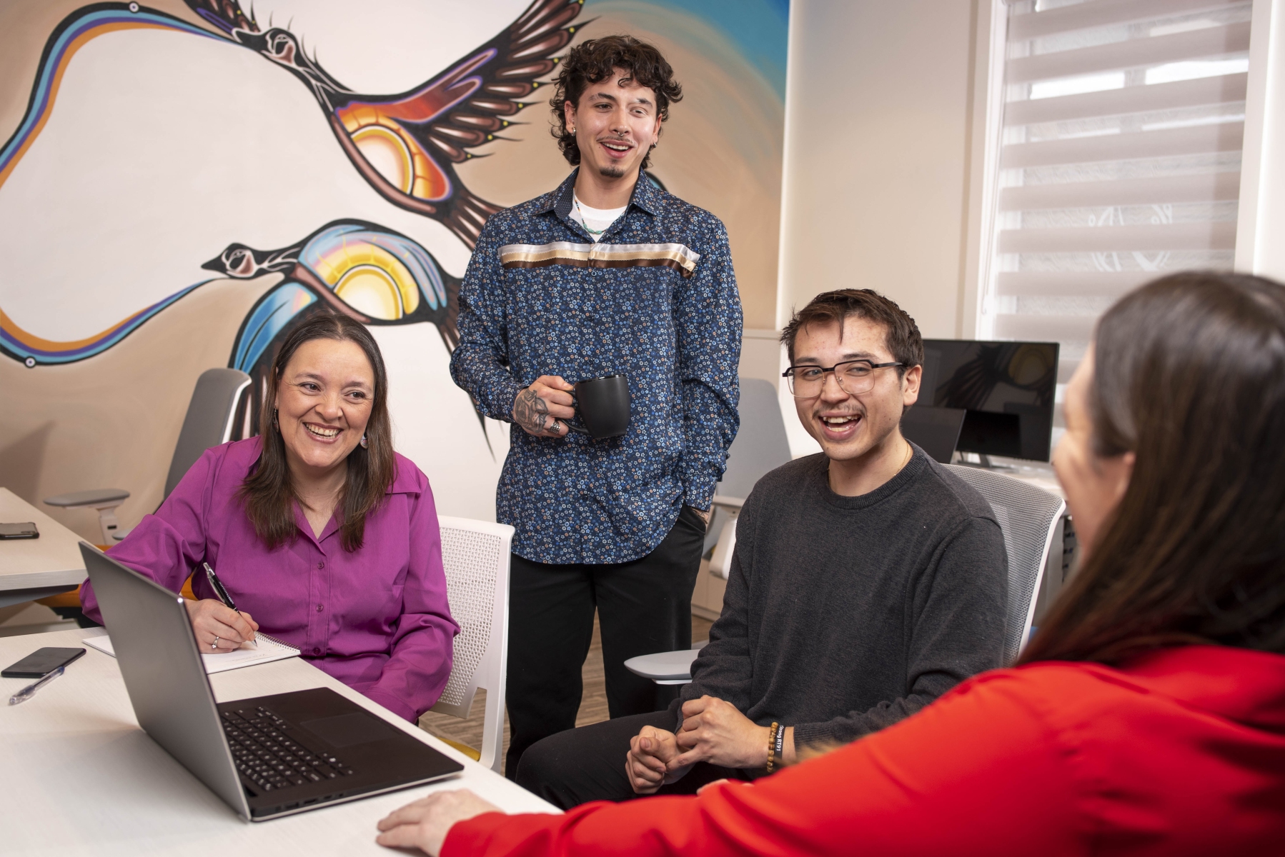 four indigenous people in an office setting smiling while they chat about a project 